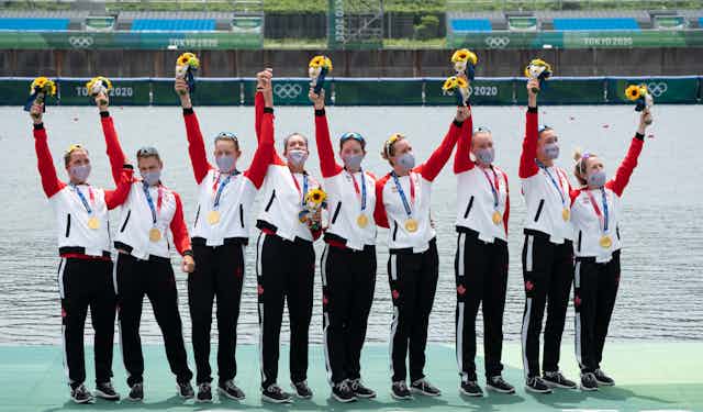 Eight rowers hold up flowers and wave to the crowd after receiving their gold medals.