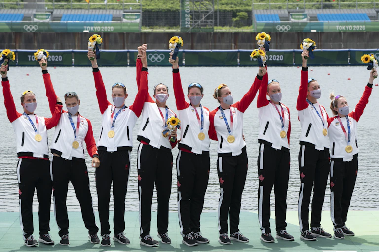 Eight rowers hold up flowers and wave to the crowd after receiving their gold medals.