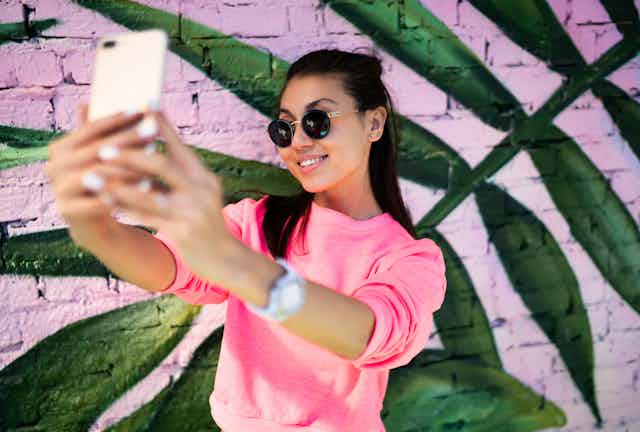 Woman taking selfie next to brightly coloured wall.