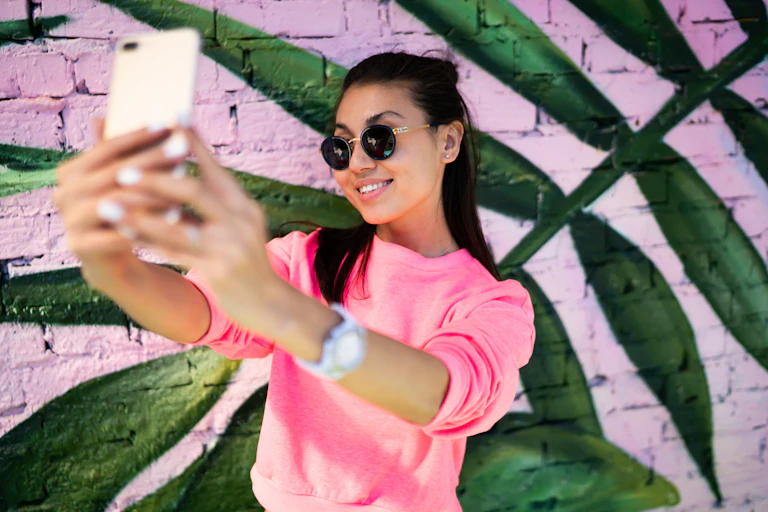 Woman taking selfie next to brightly coloured wall.
