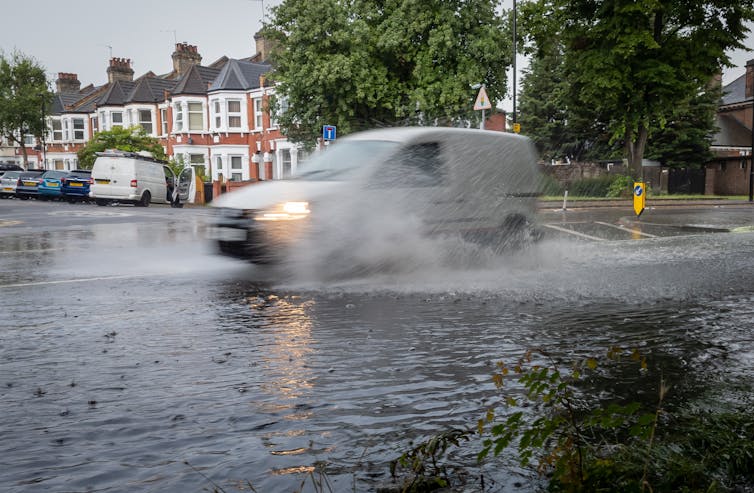 A van driving through flood water near terraced houses.