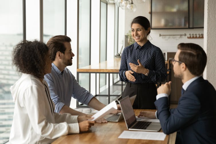 A businesswoman delivers a talk to three colleagues.