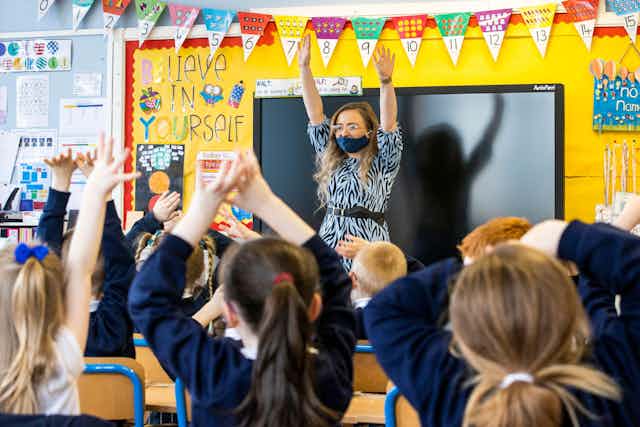 A primary school teacher raised both hands in front of a class of pupils doing the same