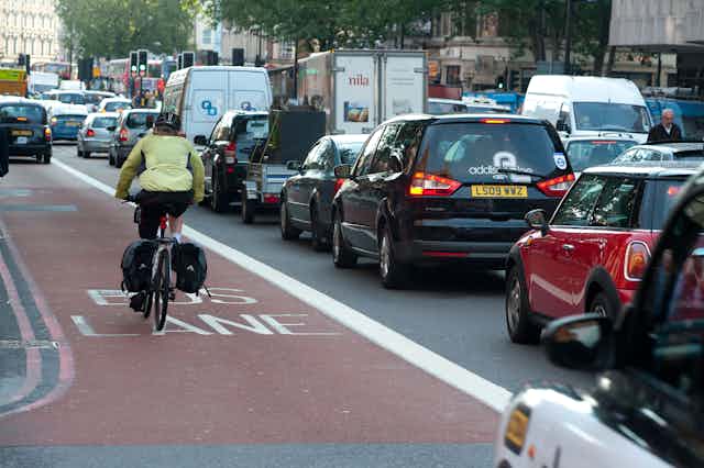 A cyclist rides down a bus lane next to a traffic jam of cars.