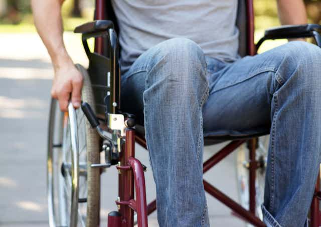 Close up photo of a man using a wheelchair in a park, showing him from the chest down.