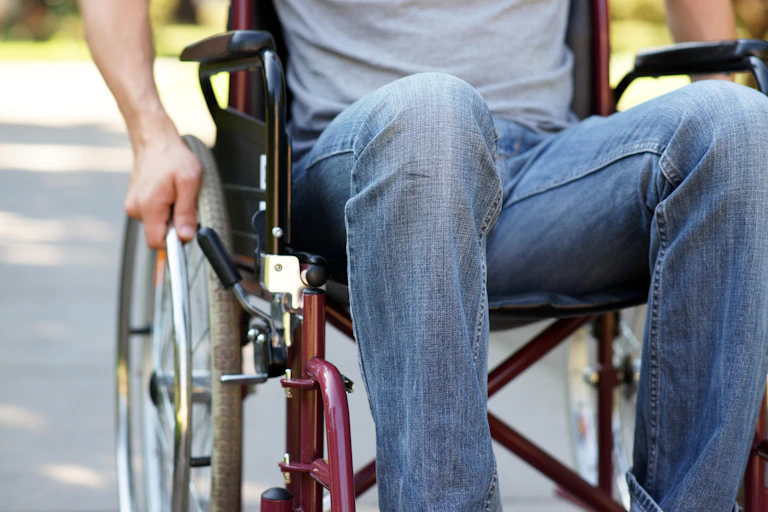 Close up photo of a man using a wheelchair in a park, showing him from the chest down.