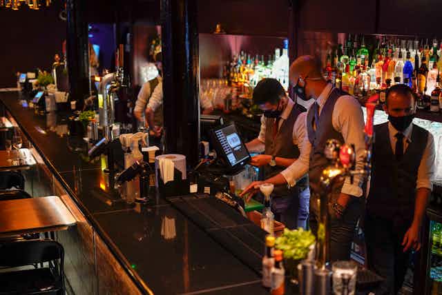 Men stand masked behind a bar