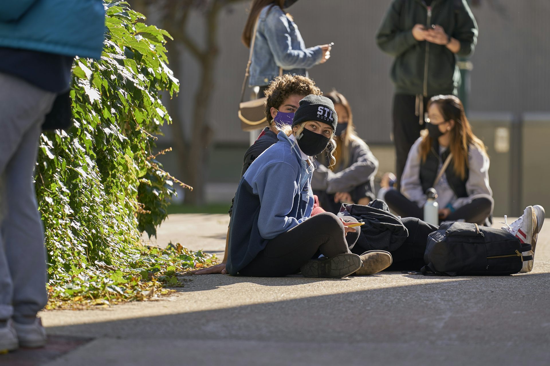 Students sit on the ground wearing face masks.