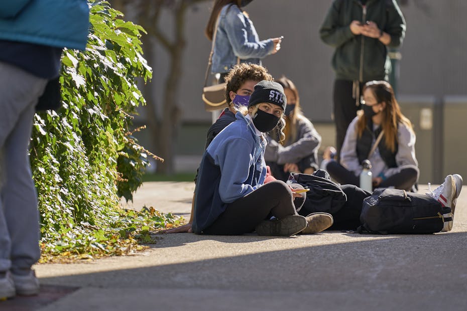 Students sit on the ground wearing face masks.
