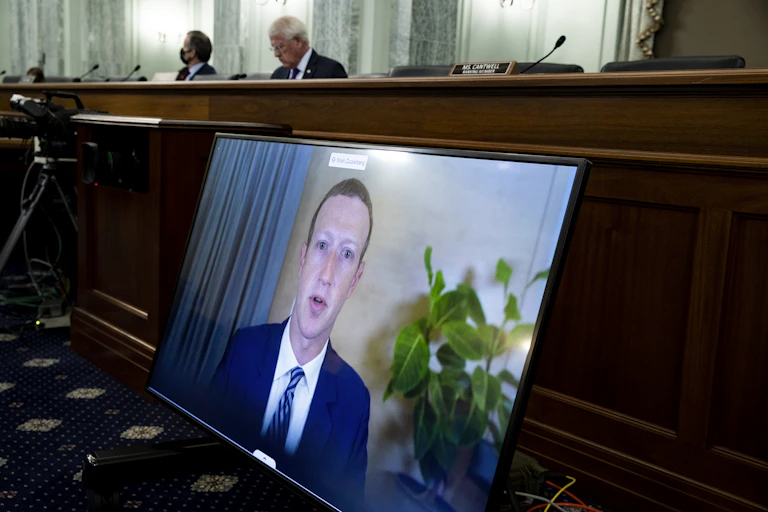 a large video screen with a man's face on it is propped against a large wooden bench behind which sit two men
