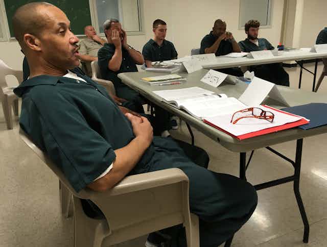 A classroom of incarcerated individuals take notes while seated.
