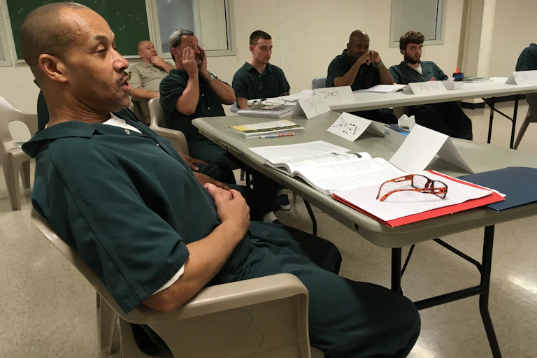 A classroom of incarcerated individuals take notes while seated.