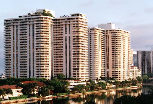 High-rise waterfront condominiums tower over tropical trees along the waterfront.