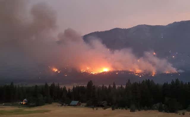 A fire burns in forested hills with homes in the foreground