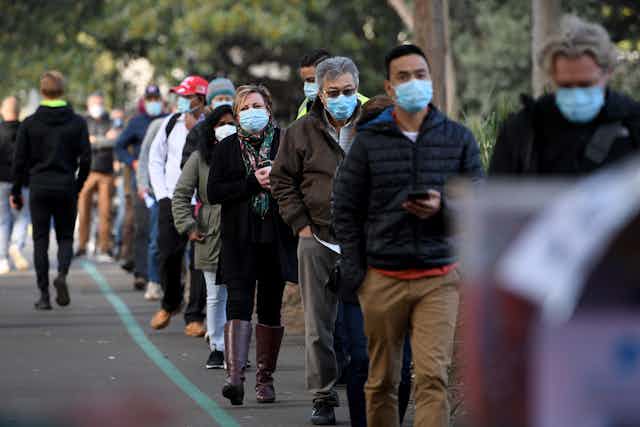 People in masks line up outside for a vaccination.