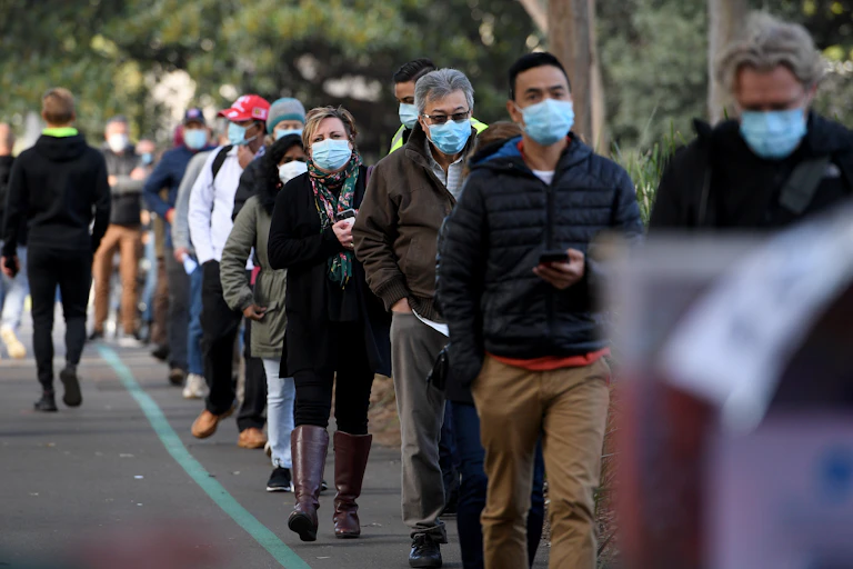 People in masks line up outside for a vaccination.