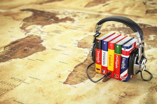 World map with dictionaries of different languages standing on it and headphones around the books.