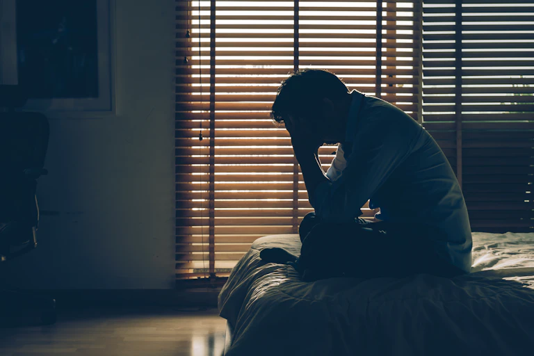 A man sitting in a darkened room hangs his head.