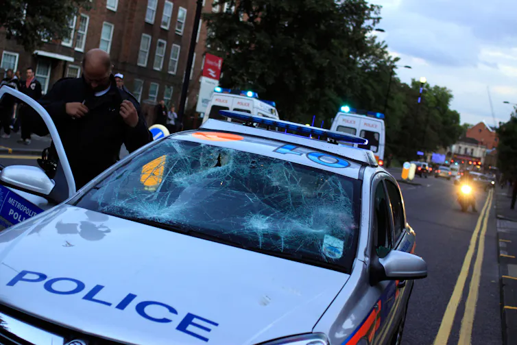 A policeman climbs into a battered police car