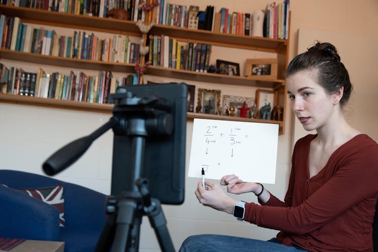 A teacher holds up a worksheet to a camera for an online lesson
