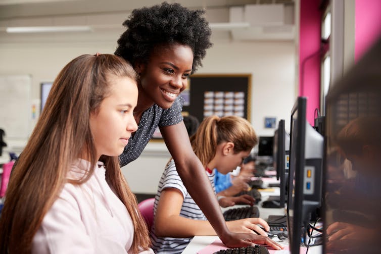 A teacher assists a female student at a computer