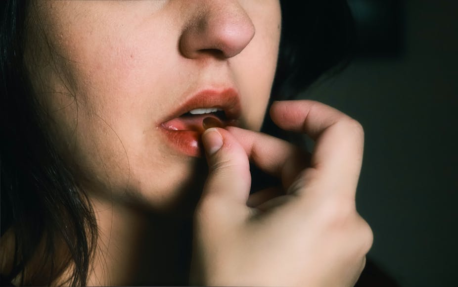 A young woman whose face is partially obscured puts a pill into her mouth.