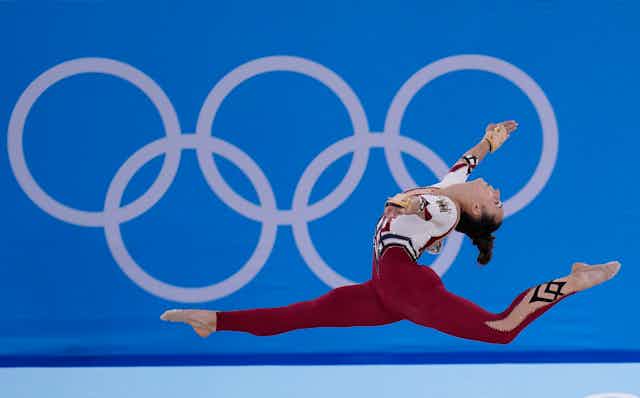 A gymnast is in the air with the Olympic rings in the background