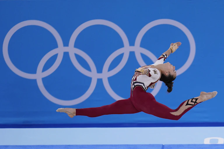 A gymnast is in the air with the Olympic rings in the background