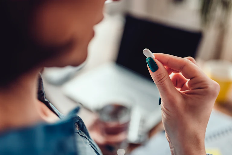 Woman wearing denim shirt sitting by the desk in the office and taking medical pills