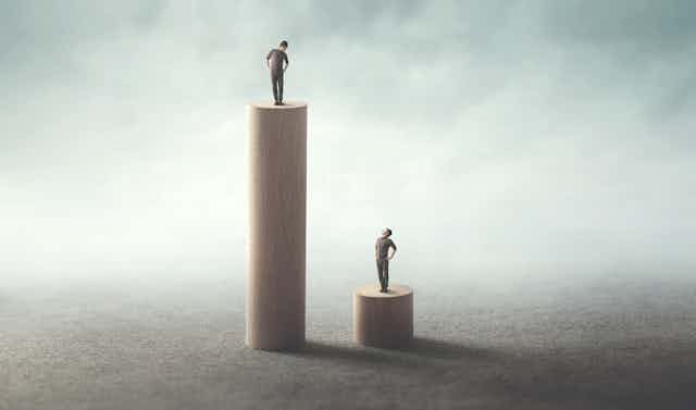Image of two men standing on different pedestals, one high and one low.