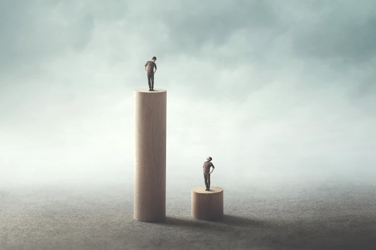Image of two men standing on different pedestals, one high and one low.