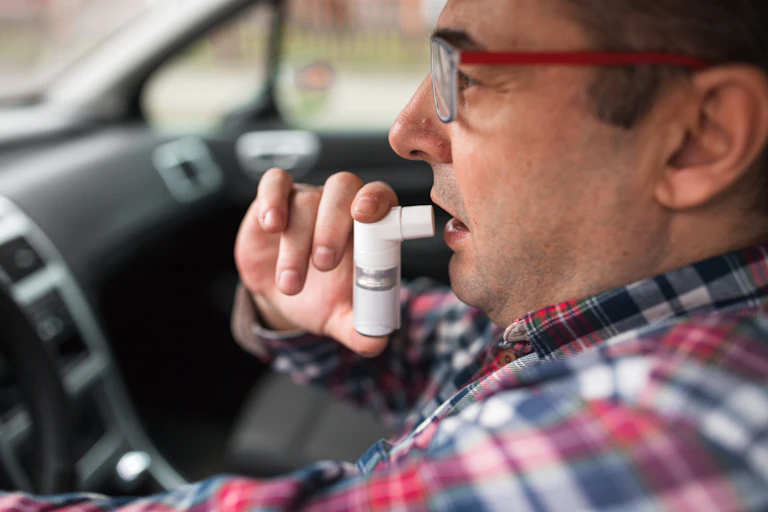 man about to use inhaler in the car