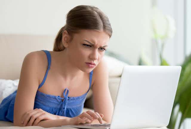 A young woman with a confused expression on her face stares at a laptop screen