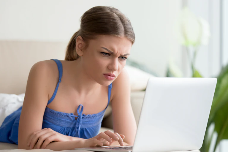 A young woman with a confused expression on her face stares at a laptop screen