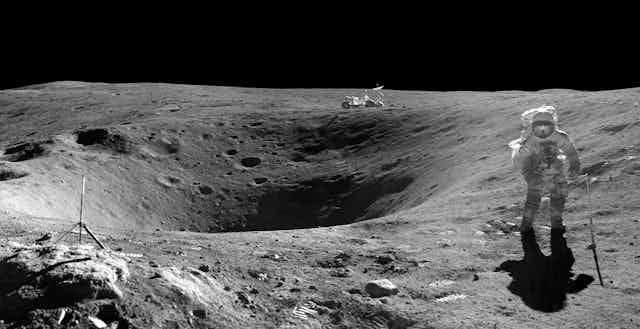 An astronaut walking on the moon with a lunar rover in the background.