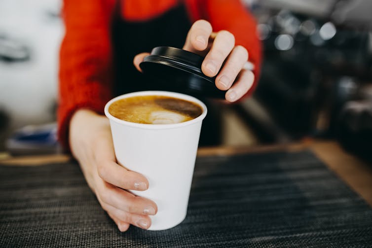 A barista puts a lid on a cup of takeaway coffee.