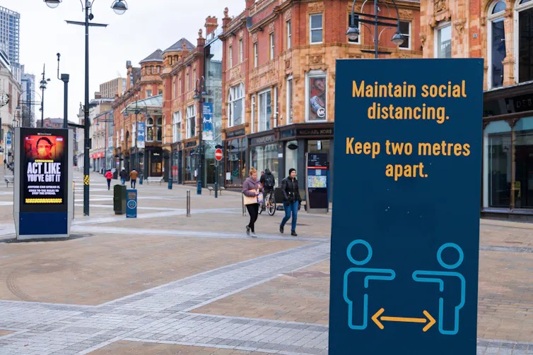 An empty high street with a panel reminding pedestrians to observe social distancing