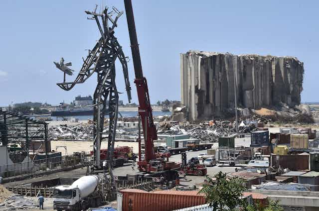A steel sculpture, memorial to people who died in the 2020 Beirut Port explosion, stands in front of the devastation of Beirut's port area.