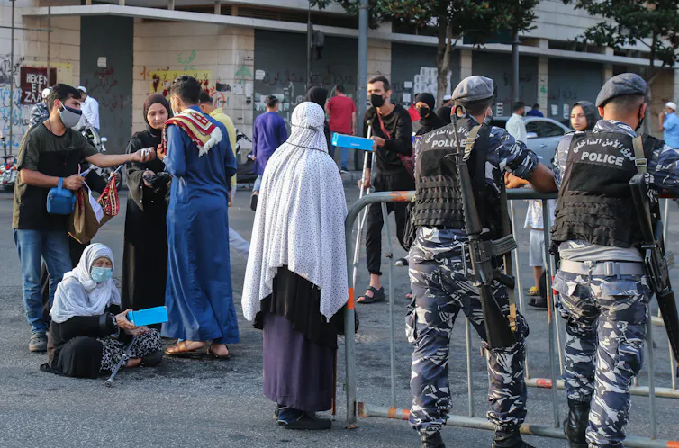 A woman walks in downtown Beirut past two members of the Lebanese security force and a woman begging.