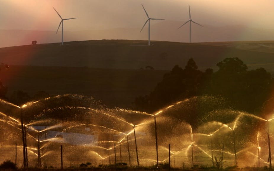 Three-armed standing structures on a hillside; water spraying from irrigation pipes in foreground