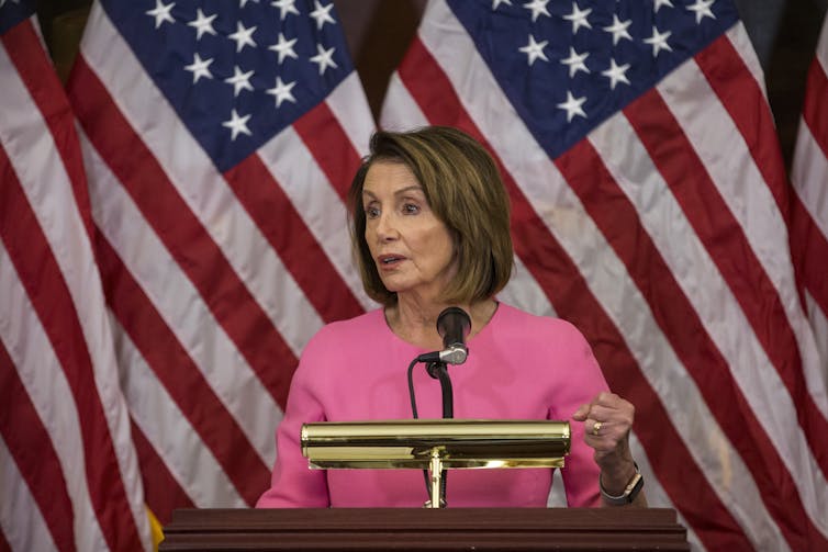 Democratic House Speaker Nancy Pelosi at a lectern in front of American flags.