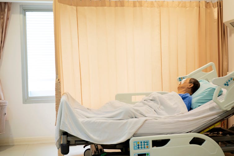 Elderly man laying in hospital bed.