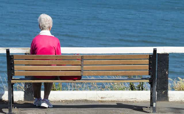 Elderly woman alone on bench, looking at the sea.