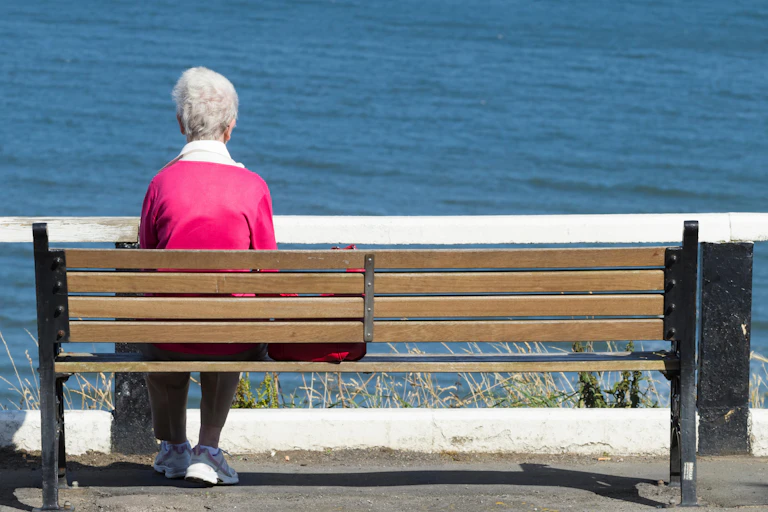 Elderly woman alone on bench, looking at the sea.