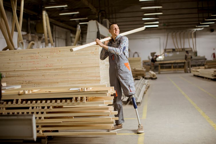 A man with an artificial leg moves lumber in a warehouse.