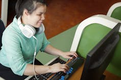 A young blind woman uses a computer with refreshable braille technology in an office setting.