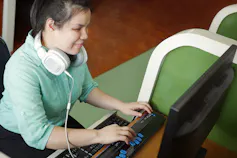 A young blind woman uses a computer with refreshable braille technology in an office setting.