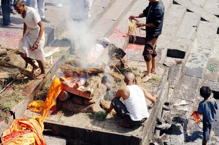 People sit and stand around a burning pyre