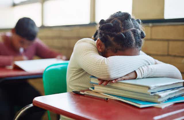 Student sits at school desk with face down on books