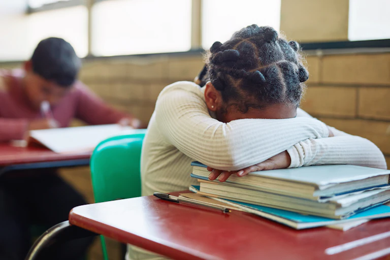 Student sits at school desk with face down on books
